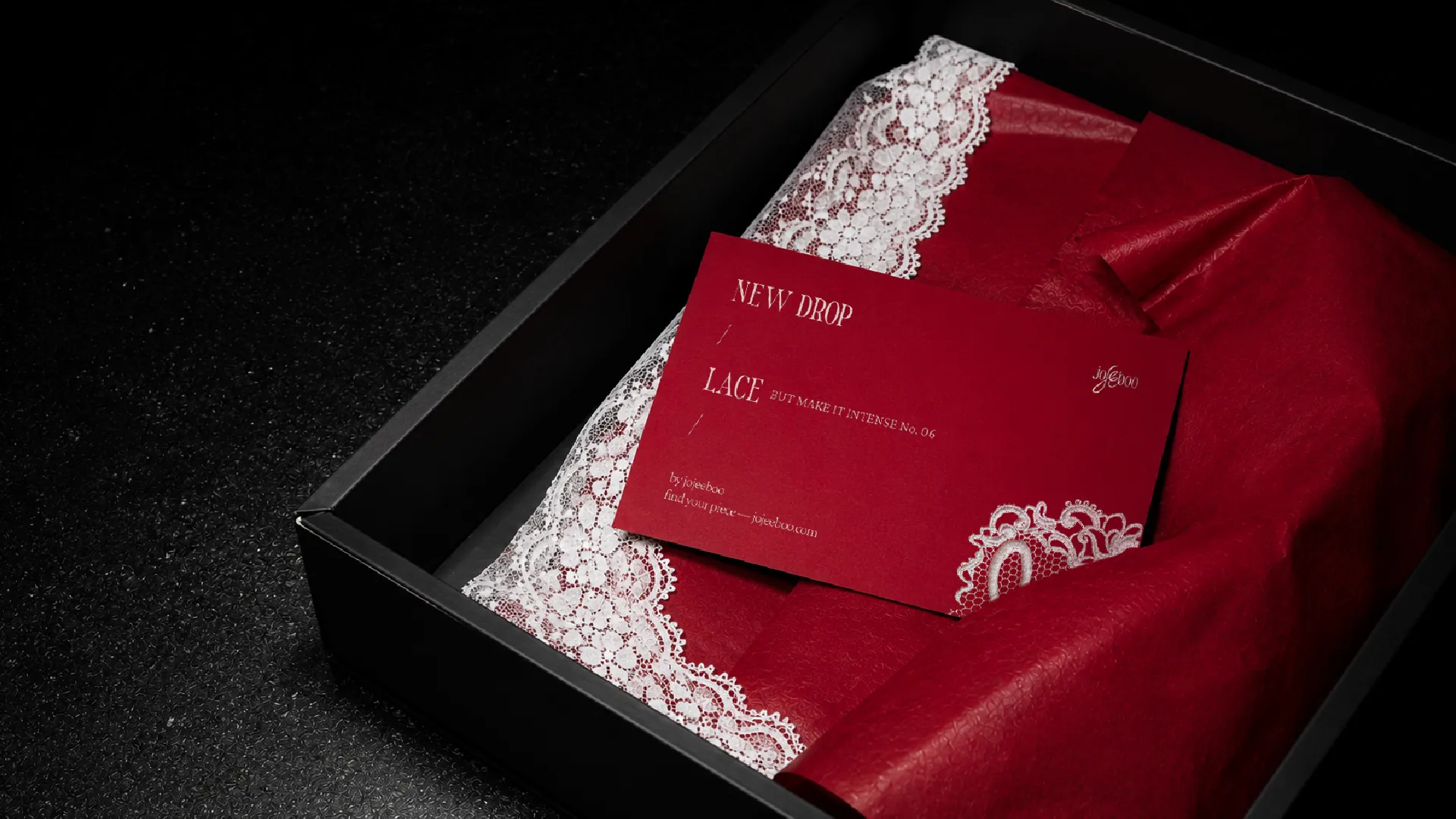 A red drop card reading new drop, lace, but make it intense, No. 06, on red tissue trimmed with white lace inside a black box