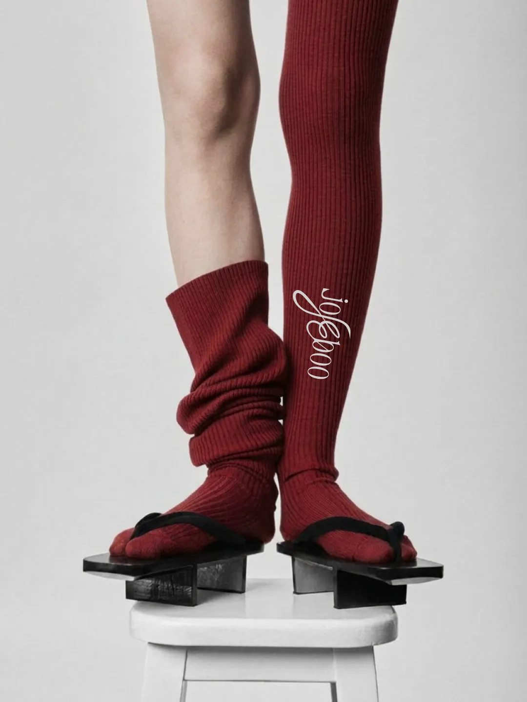Social post: legs on a white stool in wooden sandals, one burgundy sock pulled to the thigh with the wordmark running down it