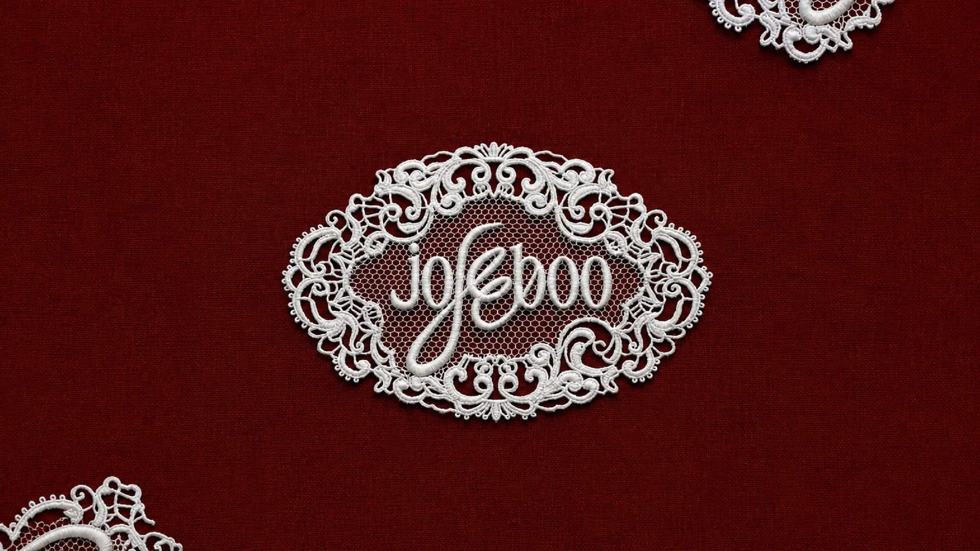 The jojeeboo wordmark inside a landscape lace cartouche, rendered as white embroidered lace on garnet fabric