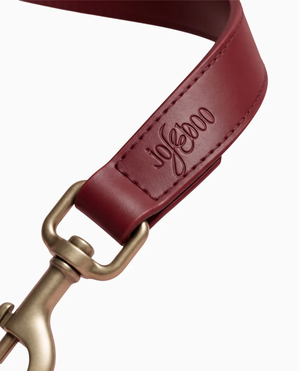 Visualisation: close up of the strap folded around a brass snap hook, the wordmark debossed on the stitched fold